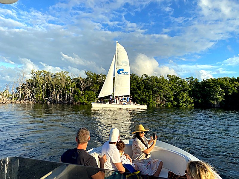 The Carolina Moon catamaran sailing past mangrove islands at golden hour as guests on a tender watch from the water in Key Largo