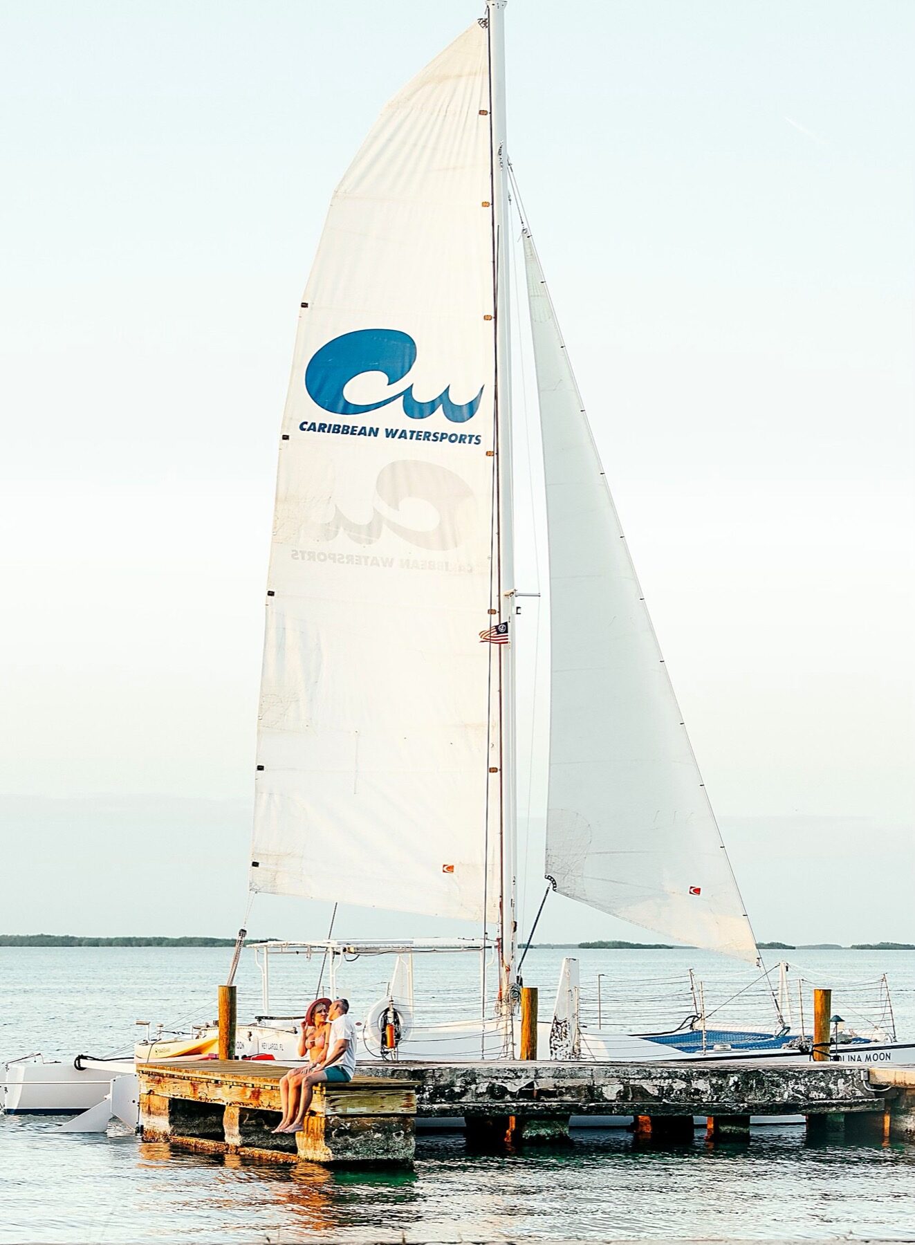 The Carolina Moon catamaran with the blue Caribbean Watersports logo on its mainsail, moored off a Key Largo dock