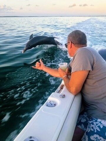 A guest watching a wild dolphin leap alongside the boat at sunset on a Key Largo dolphin tour