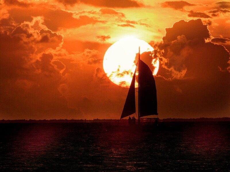 A sailing catamaran silhouetted against a blazing orange Key Largo sunset