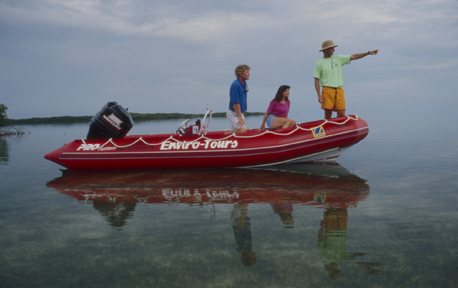 A guide pointing out wildlife to a family aboard the red Enviro-Tours boat on calm water