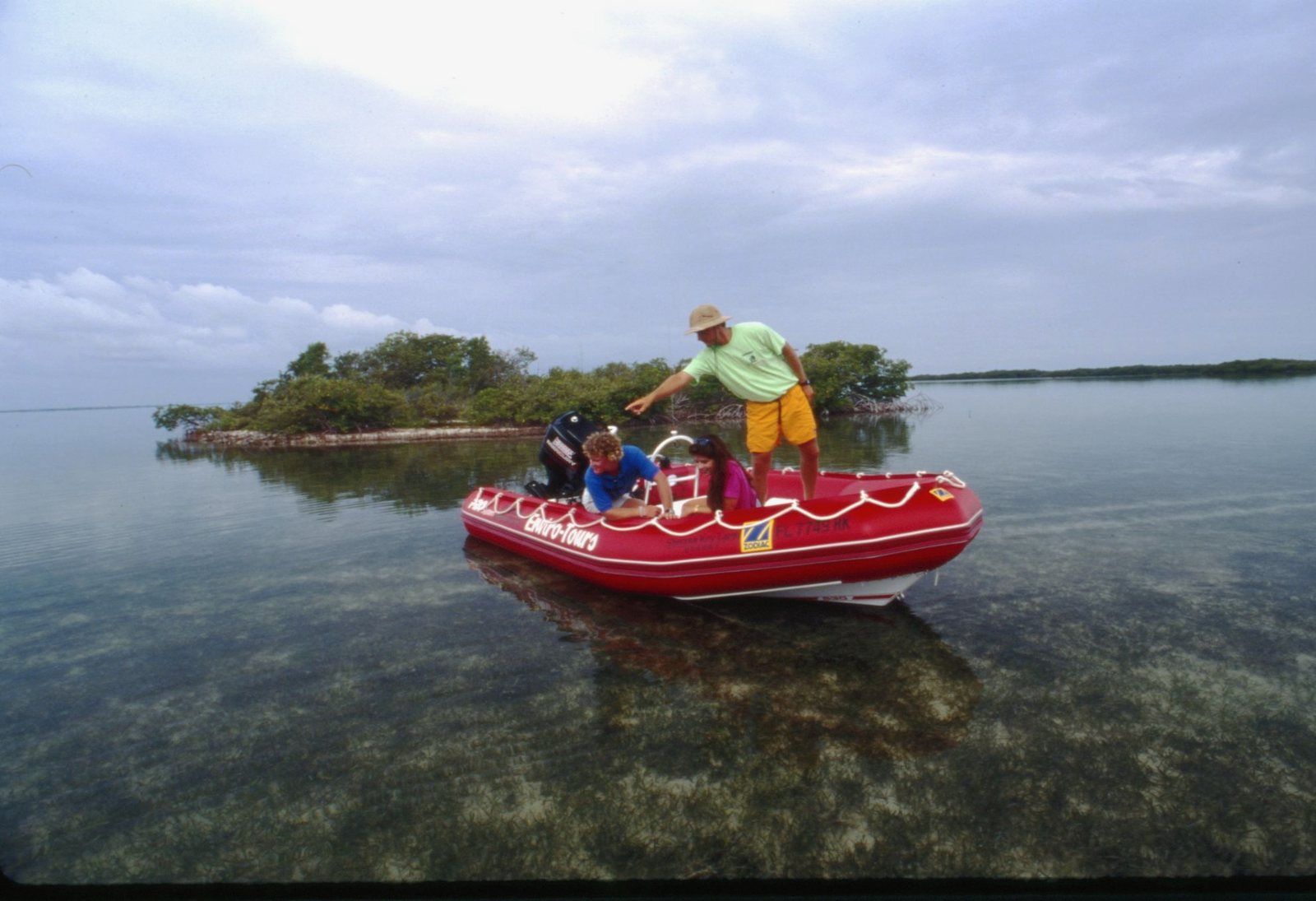 A guide standing in the red Enviro-Tours boat beside a small mangrove island on glassy water