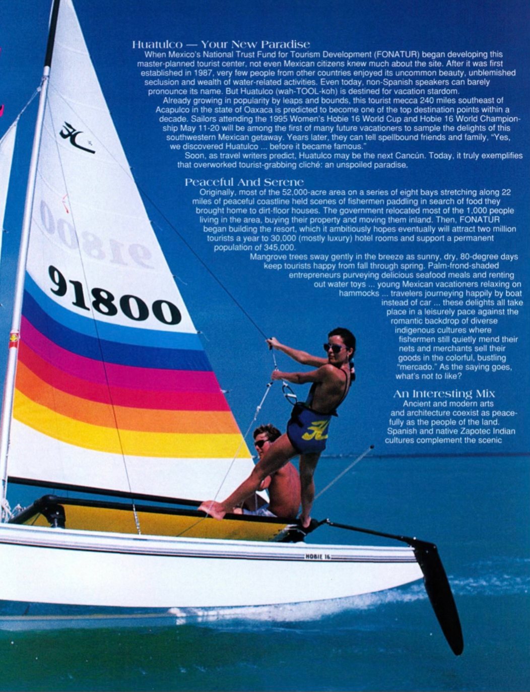 A sailor leaning out from a Hobie catamaran with a full rainbow-striped sail