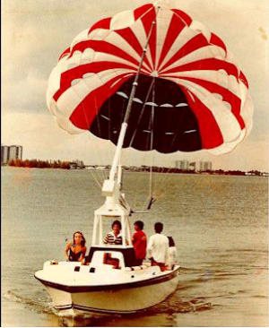 A red and white parasail lifting off behind a small boat in an early film photograph
