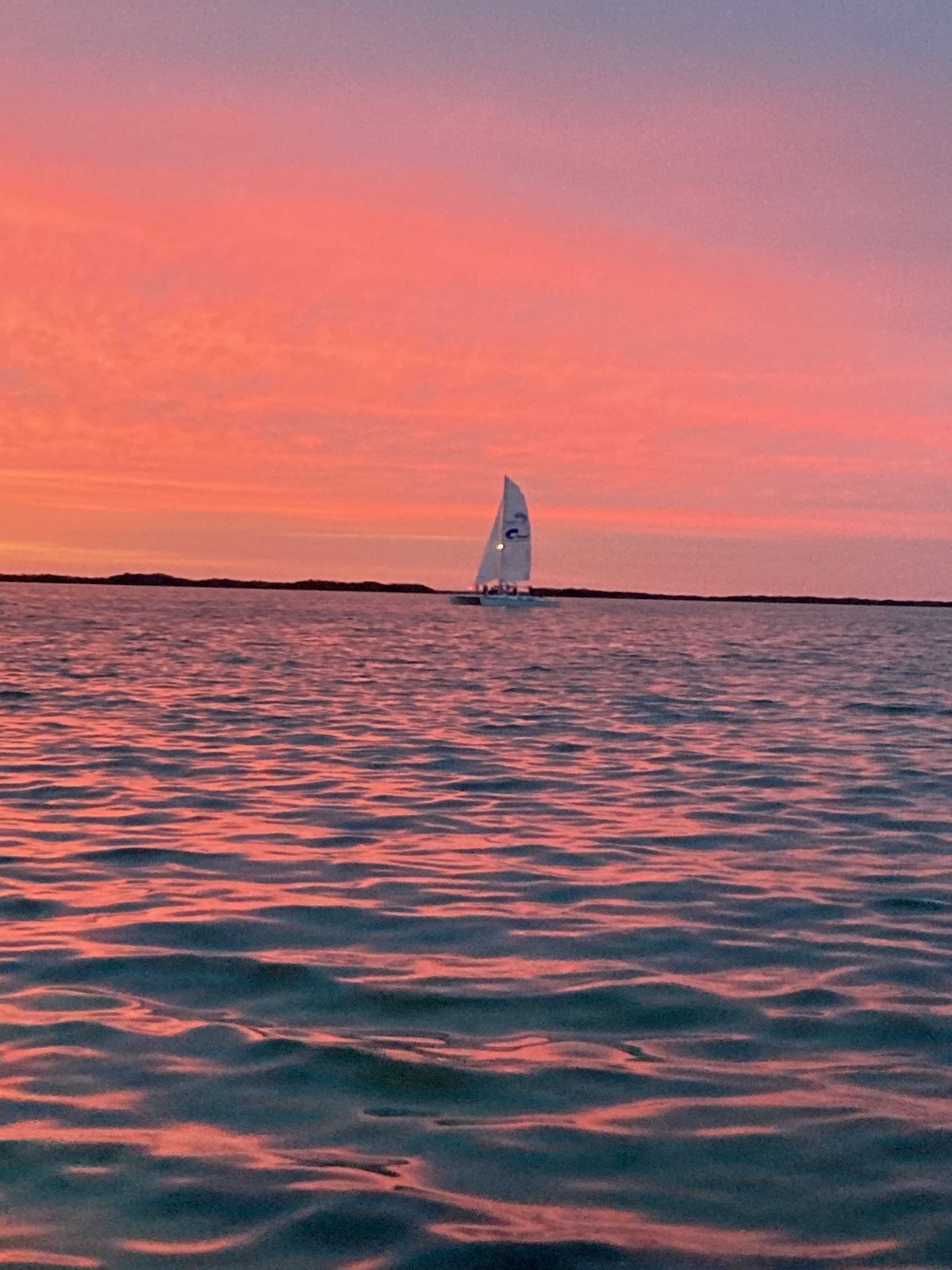 A lone sailboat on glassy water under a pink and lavender sunset sky